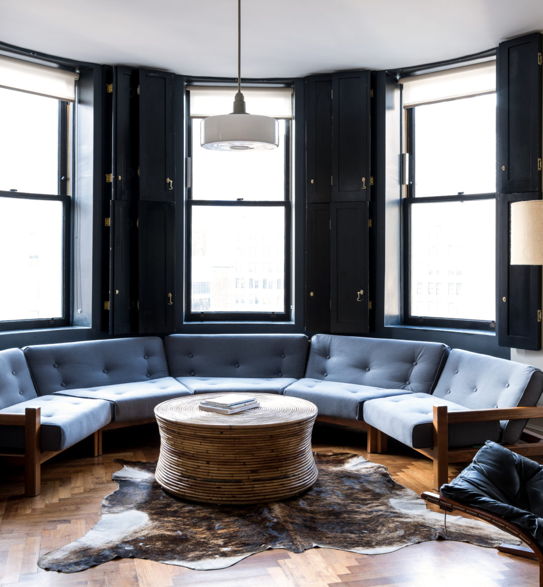 A semi-circular sofa sits under 3 windows with striking views of Midtown Manhattan
