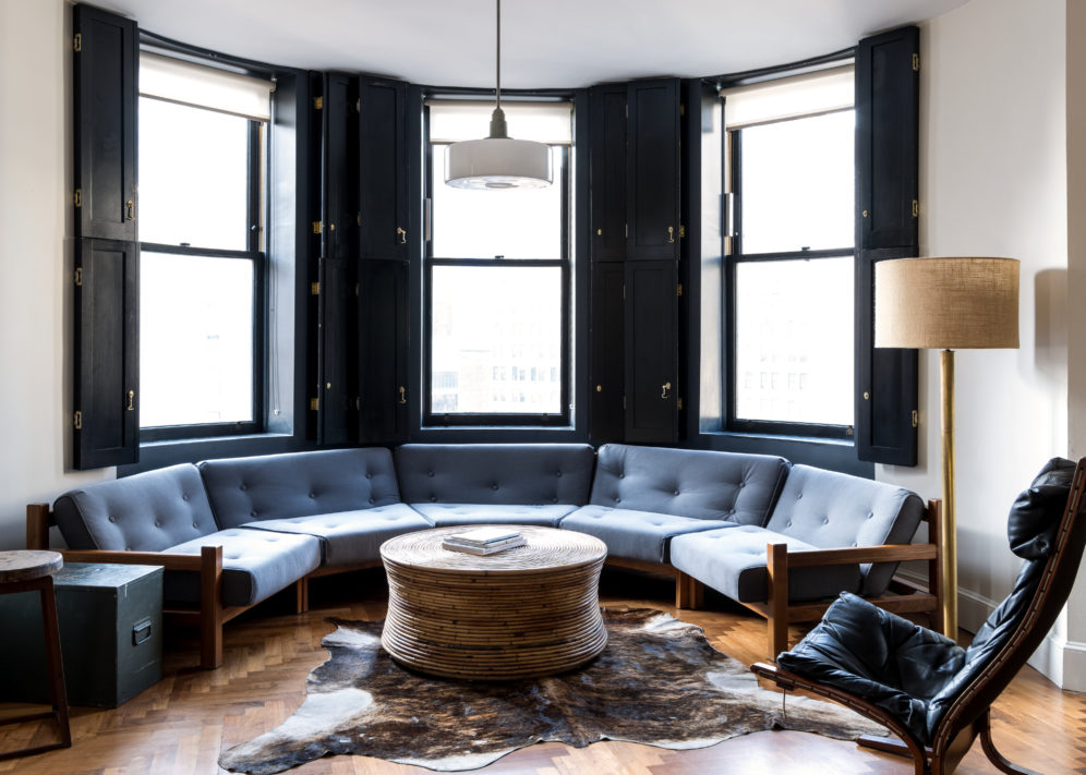 A semi-circular sofa sits under 3 windows with striking views of Midtown Manhattan