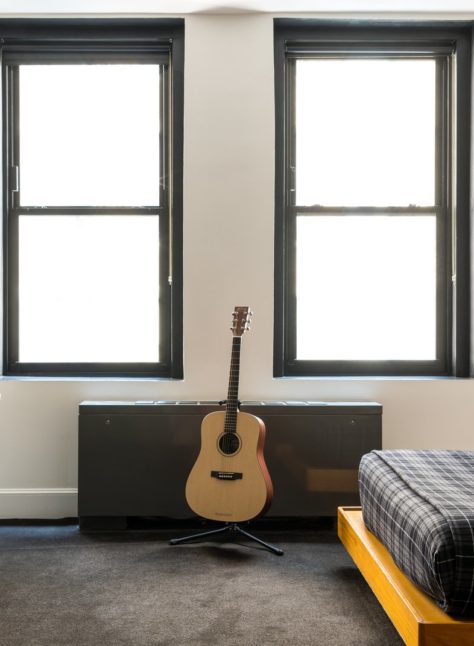 A room with dark carpets features 2 windows and a corner desk with multiple chairs