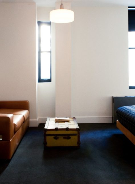 A room with dark carpets features two windows and a brown leather sofa