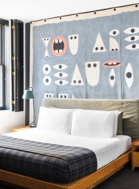 A bed is drenched in natural light flooding in from a window with stylish black, wooden indoor shutters
