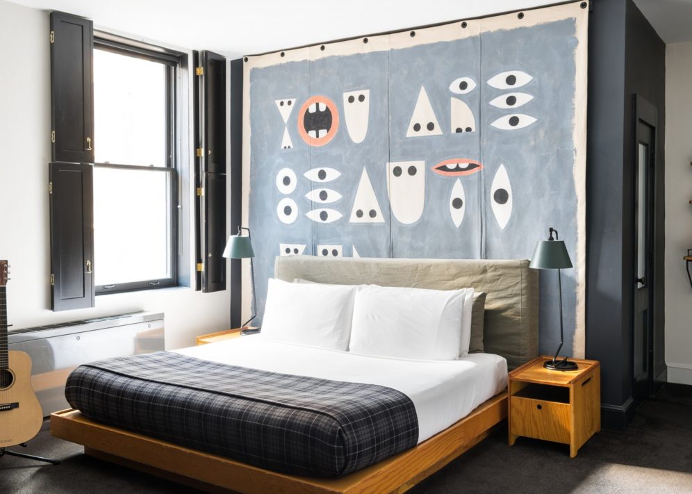 A bed is drenched in natural light flooding in from a window with stylish black, wooden indoor shutters