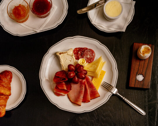 Breakfast served on dining plate with selection of cheeses, croissants and juices.