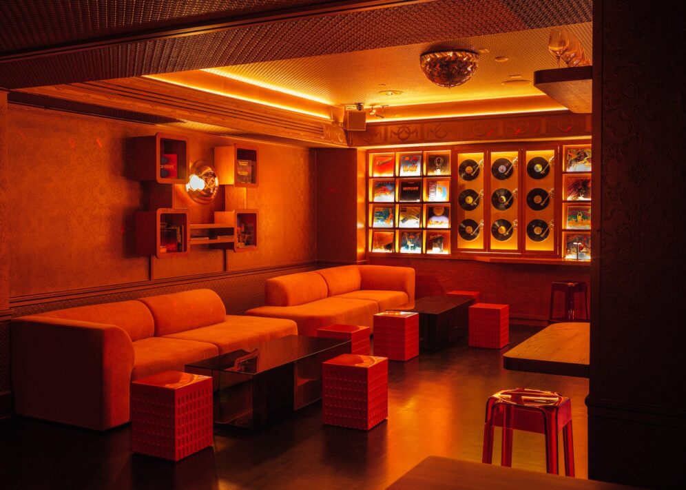 Libera corner sofa dining area with orange lit lights, vinyl record background wall and small tables.