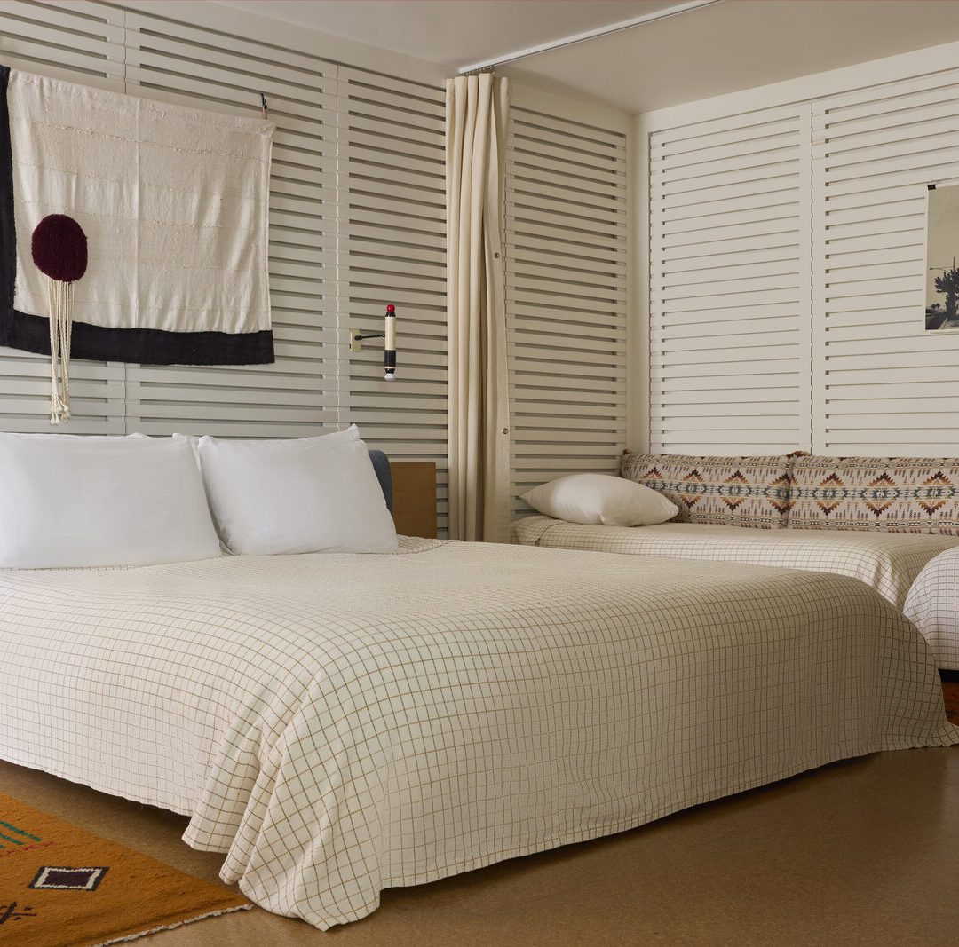 A large bed sits in the middle of the room, flanked by a radio on one side and twin beds against a wall on another