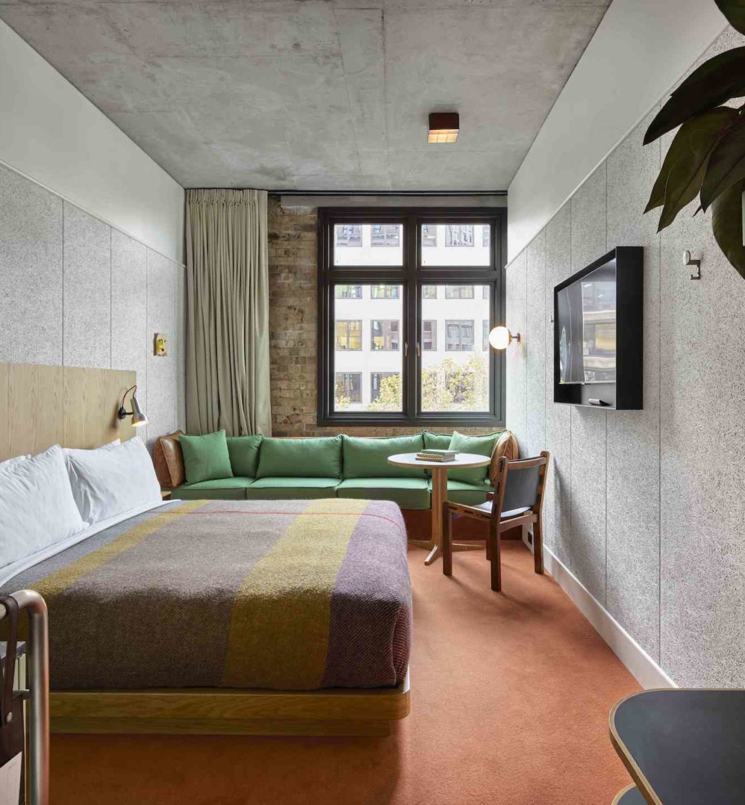 A modern room with red carpeting features a green couch against an exposed brick wall