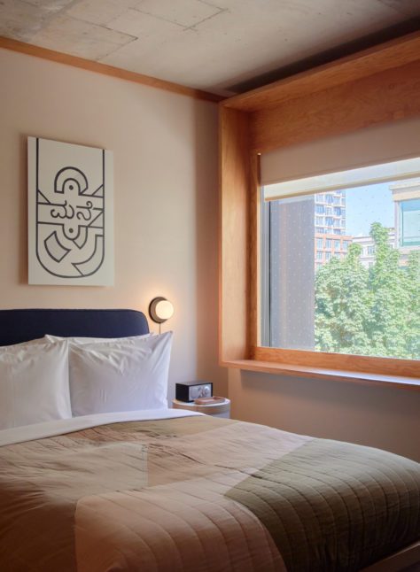 A bed sits next to a wall featuring two windows and a black leather seating area