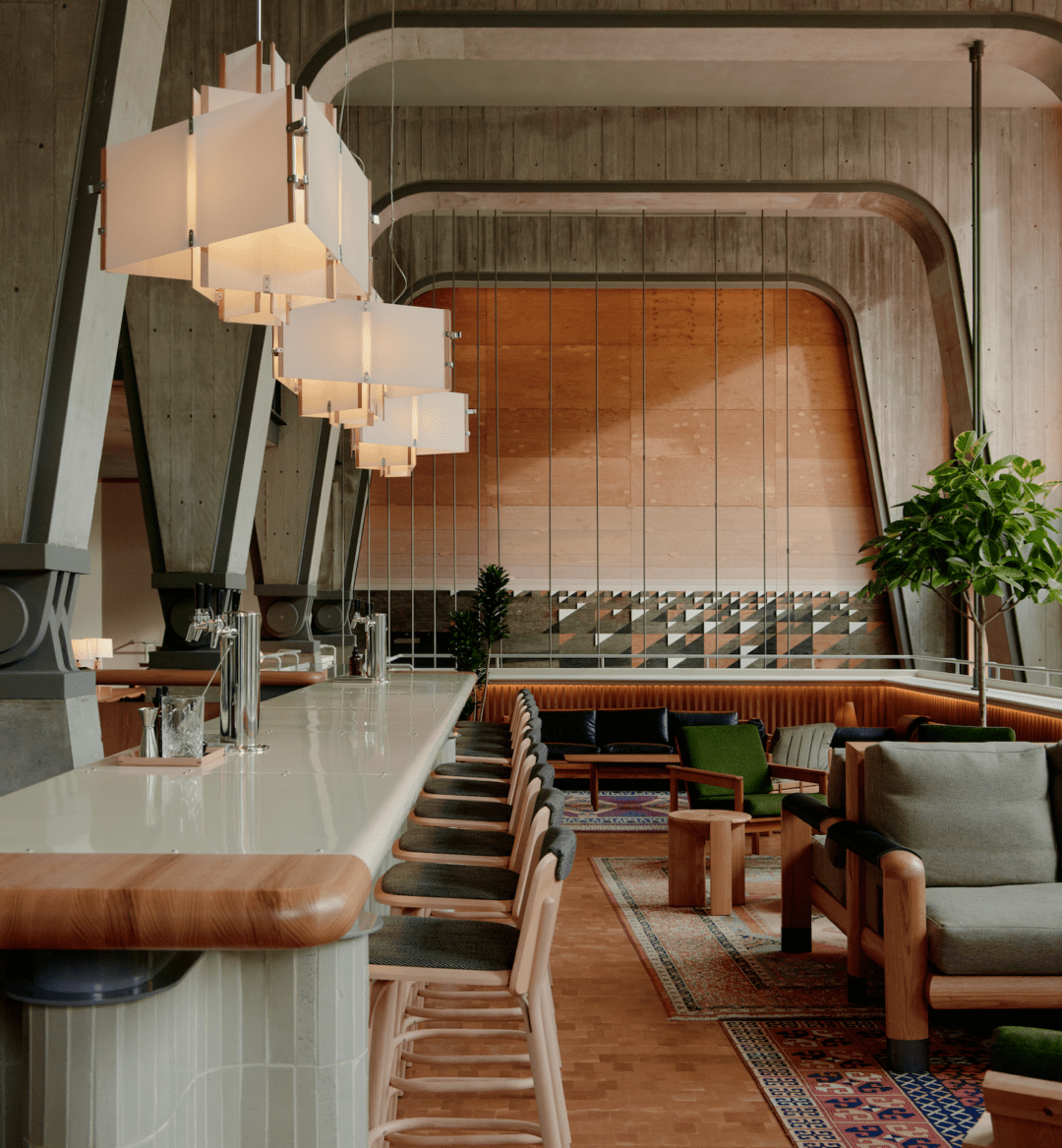 Modern cafe interior with a long bar, wooden chairs, pendant lights, and green lounge seating under large arched concrete beams.